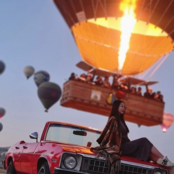 Vintage Car Photoshoot with Balloons A vintage classic car parked in front of hot air balloons rising over Cappadocia at sunrise.